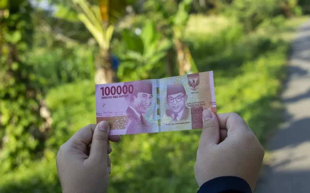 Hand holding an Indonesian 100,000 rupiah banknote, representing transparent fees